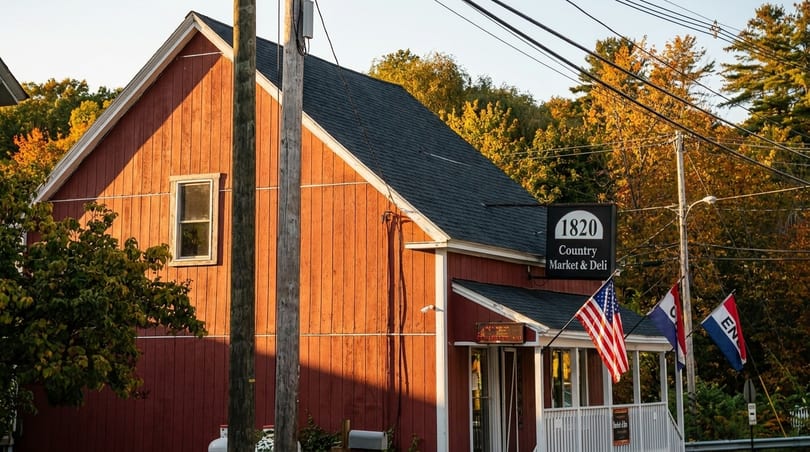Red wooden building of "1820 Country Market & Deli" with American flags, surrounded by autumn trees.