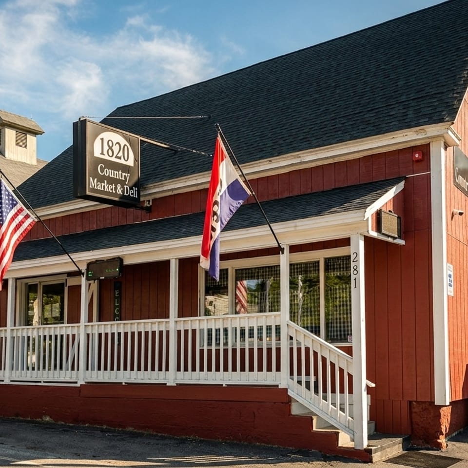 The red 1820 Country Market & Deli building with a white porch and flags under a blue sky.