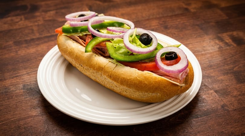 A submarine sandwich with ham, cheese, lettuce, tomatoes, green peppers, red onions, and olives.